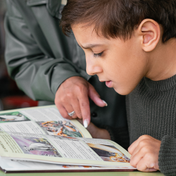 Child reading a book with a parent pointing at a page